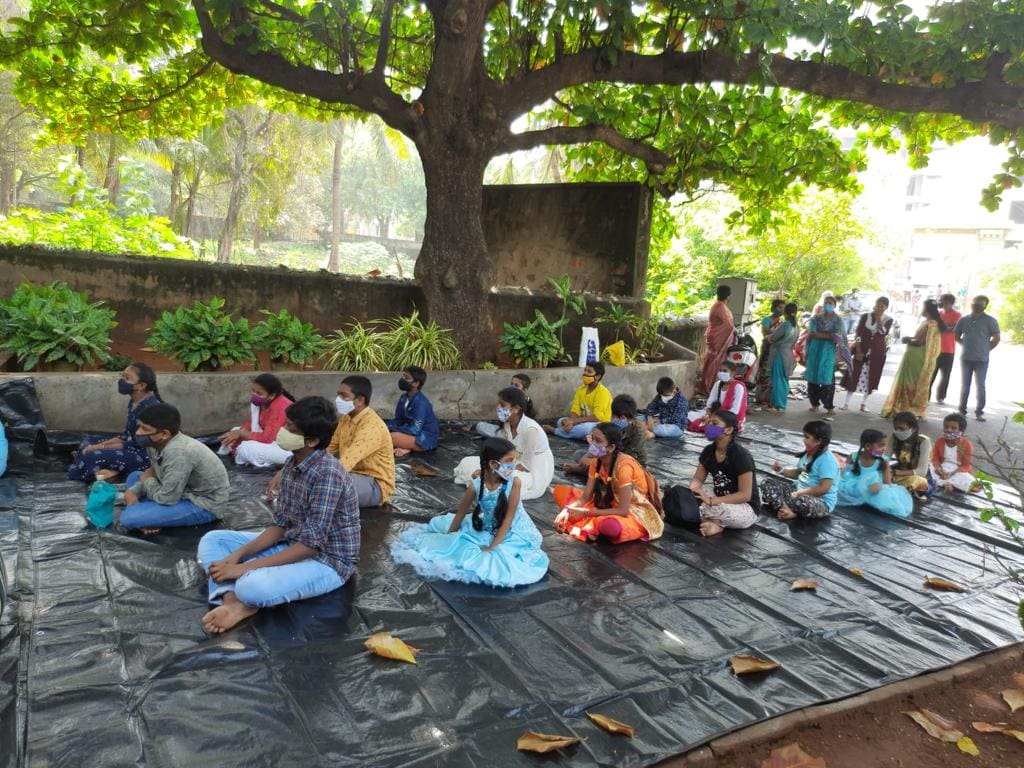 People sitting on the ground, eating food together under a large tree.