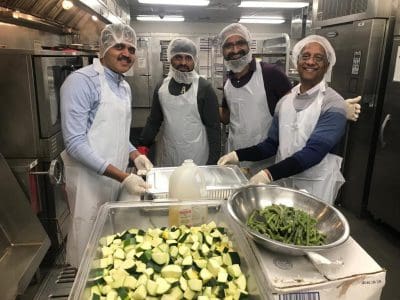 Four men in aprons preparing vegetables in a kitchen.