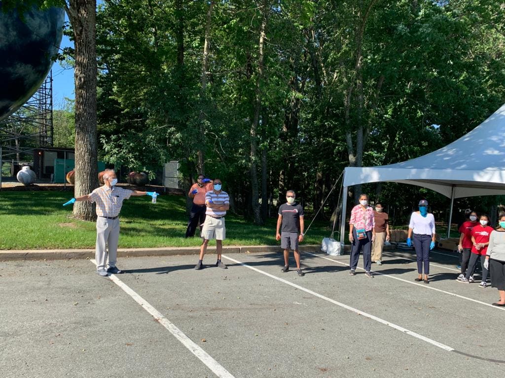 People socially distanced outdoors near a tent and trees.