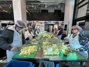 Smiling volunteers slicing lettuce at communal prep table